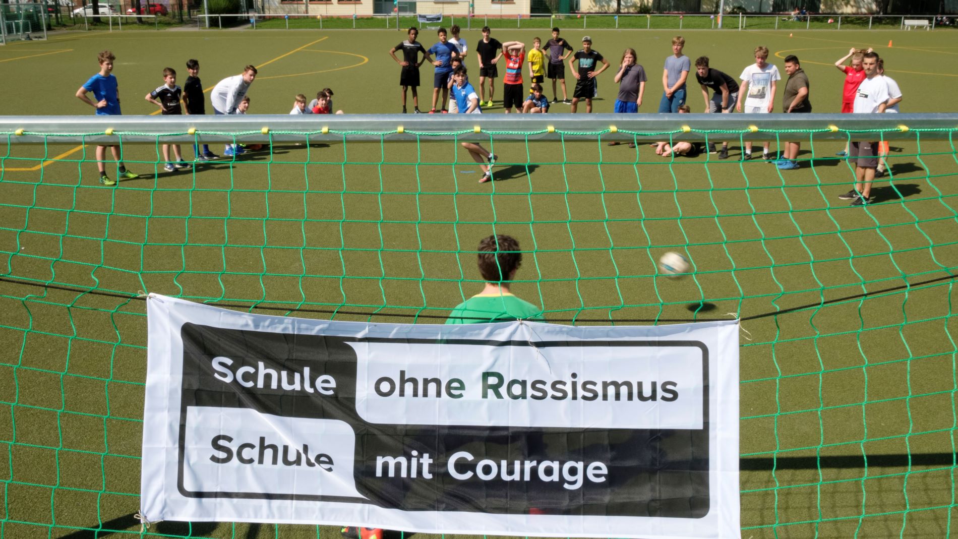 Eine Gruppe von Schüler*innen spielt Fußball. Am Tor ist ein SOR-SMC Plakat aufgehängt.